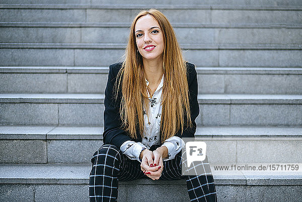 Porträt einer lächelnden jungen Frau  die auf einer Treppe sitzt