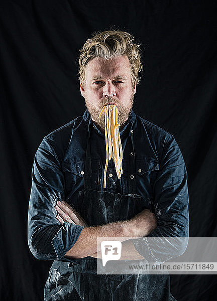 Hobby chef holding fresh tagliatelle pasta in his mouth