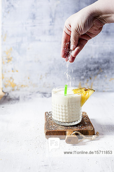 Frau streut Kokosnussflocken auf einen Ananas-Kokos-Smoothie