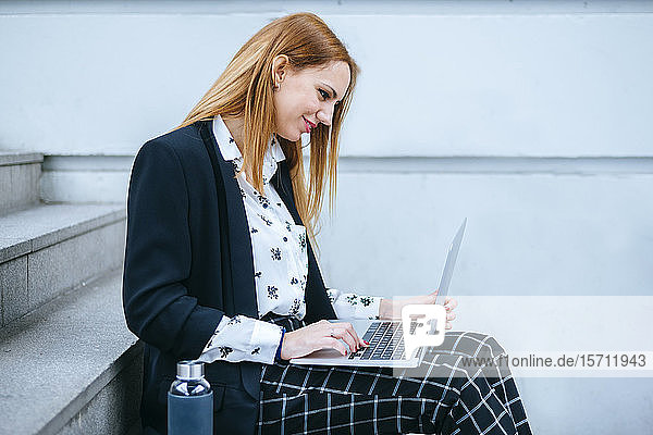 Junge Geschäftsfrau sitzt mit Laptop auf der Treppe