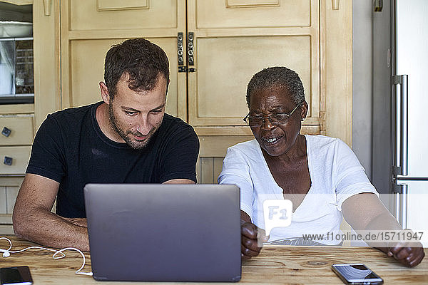 Ältere Frau und Mann sitzen am Küchentisch und teilen sich einen Laptop