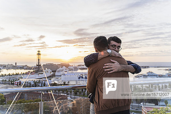 Schwules Paar umarmt sich auf einem Aussichtspunkt über der Stadt mit Blick auf den Hafen,  Barcelona,  Spanien