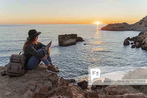 Junge Frau benutzt Smartphone am Strand bei Sonnenuntergang Ibiza
