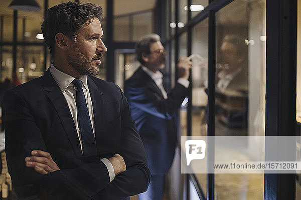 Portrait of confident businessman with colleague drawing on glass pane in office