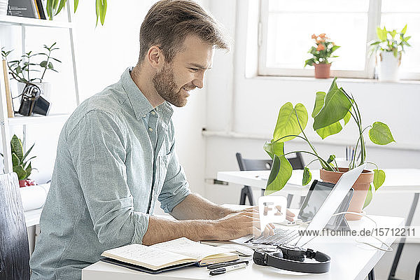 Smiling man using laptop at desk in office