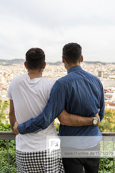 Rückenansicht eines schwulen Paares  das Arm in Arm auf die Stadt blickt  Barcelona  Spanien