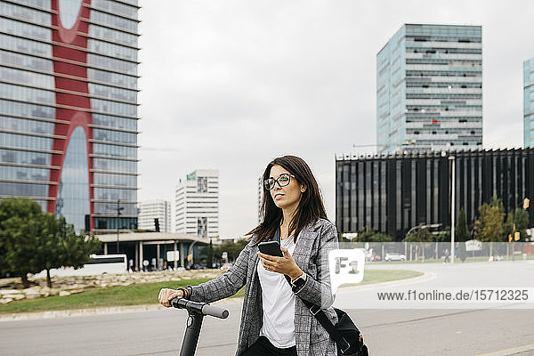 Junge Geschäftsfrau mit Smartphone auf einem E-Scooter in der Stadt