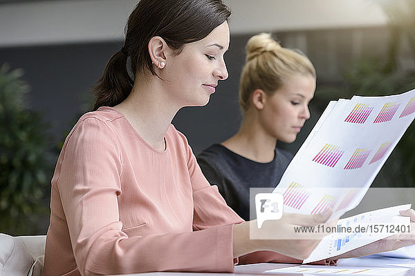 Young businesswoman with colleague reading documents in office
