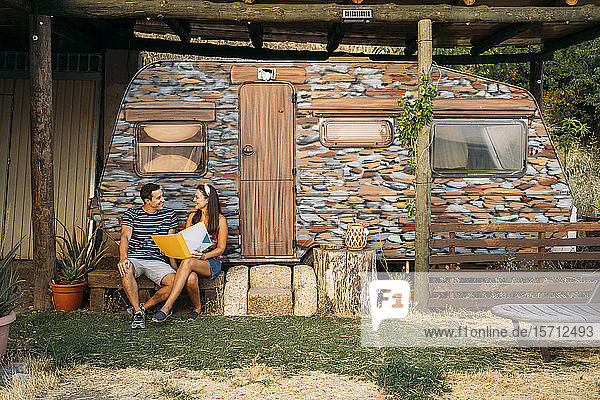Mann und Frau mit einer Mappe sitzen an einem bemalten Wohnwagen