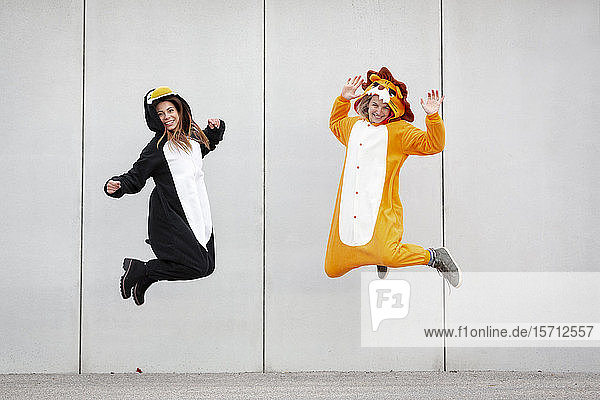 Zwei Frauen in Pinguin- und Löwenkostüm springen vor Betonmauer