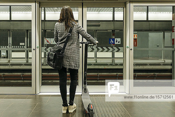 Rear view of young businesswoman with e-scooter waiting for the subway at a station