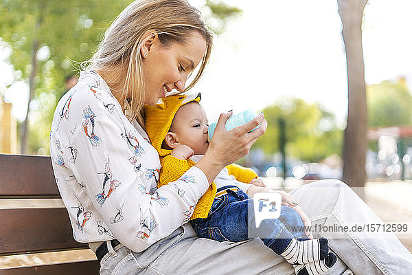 Mother bottle-feeding baby boy on a park bench