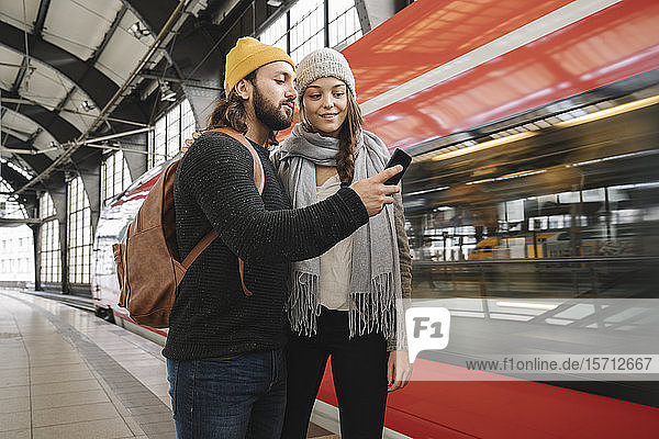 Young couple using smartphone at the station platform as the train comes in  Berlin  Germany