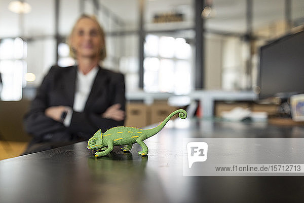 Mature businesswoman with chameleon figurine on desk in office