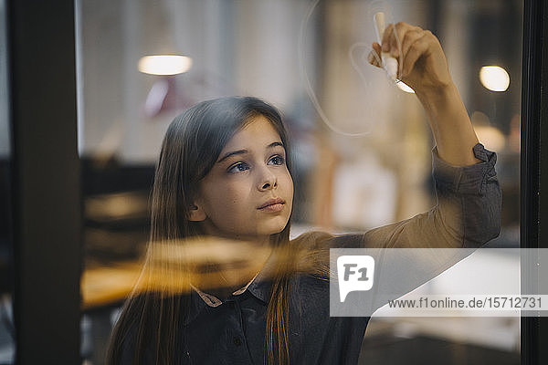 Girl drawing on glass pane in office