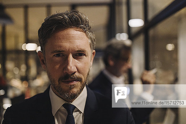 Portrait of confident businessman with colleague drawing on glass pane in office