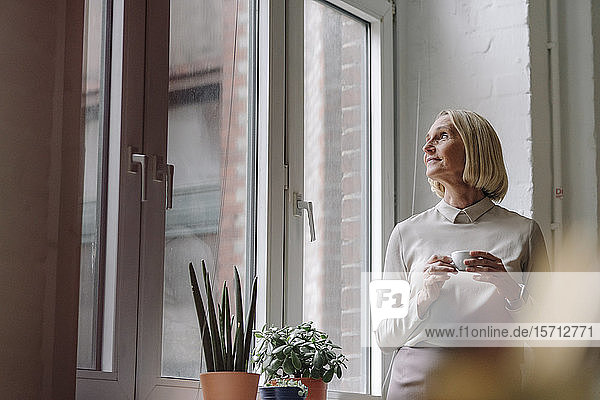 Mature businesswoman having a coffee break at the window in office