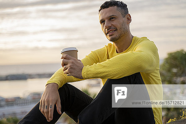 Mann sitzt bei Sonnenuntergang mit Kaffee zum Mitnehmen im Freien