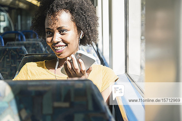 Happy young woman with earphones and smartphone on a train