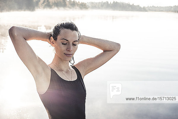 Frau im schwarzen Badeanzug an einem See im Morgennebel