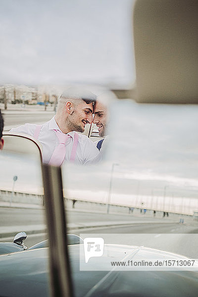 Reflection in rear view mirror of an elegant gay couple in a vintage convertible car
