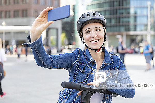 Lächelnde Frau mit E-Scooter beim Selbstfahren in der Stadt  Berlin  Deutschland