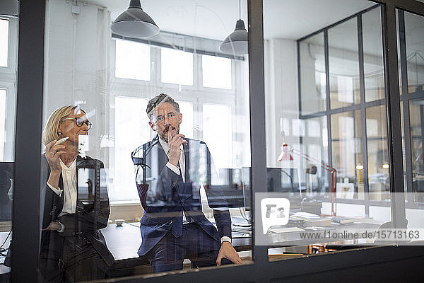Businessman and businesswoman looking at drawing on glass pane in office