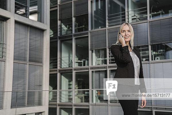 Blonde Geschäftsfrau mit Smartphone im Hintergrund modernes Gebäude