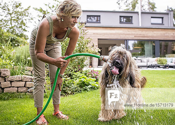 Frau mit Hund und Gartenschlauch im Garten