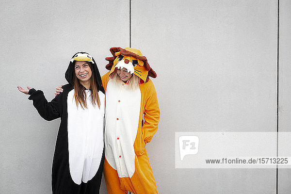 Two women in penguin and lion costume in front of concrete wall