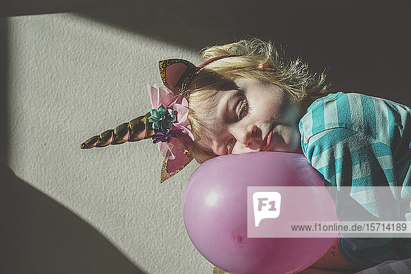 Porträt eines kleinen blonden Mädchens mit Einhornhorn  das sich an einen rosa Ballon lehnt