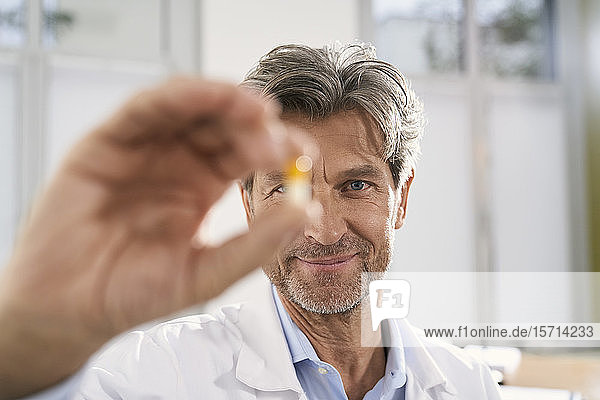 Porträt eines Arztes  der in seiner Praxis eine Kapsel hält