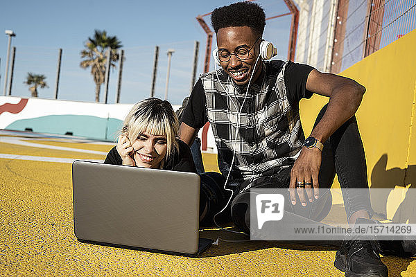 Porträt eines lächelnden jungen Paares mit Kopfhörer und Laptop im Freien