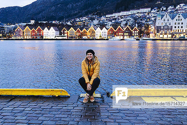 Frau mit gelber Jacke sitzt im Hafen von Bergen  Norwegen