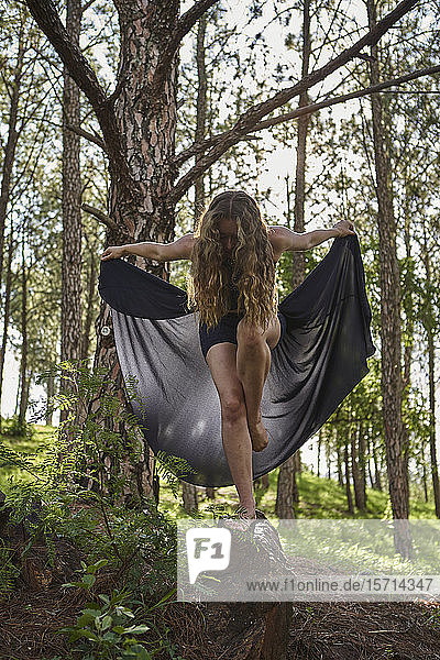 Barfüssige junge Frau steht auf einem Bein auf einem Felsen im Wald
