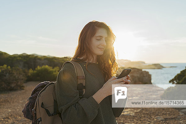 Rothaarige junge Frau telefoniert bei Sonnenuntergang an der Küste  Ibiza  Spanien