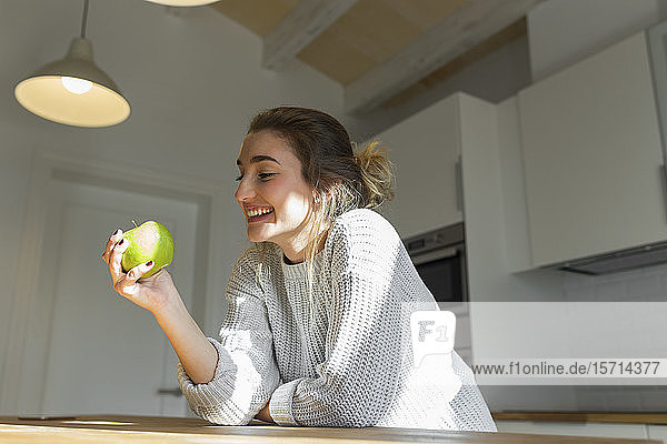 Junge lächelnde Frau hält grünen Apfel in der Küche