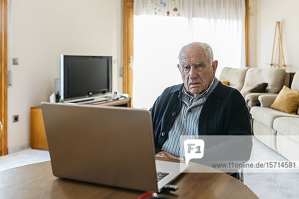 Portrait of content senior man in wheelchair with laptop at home