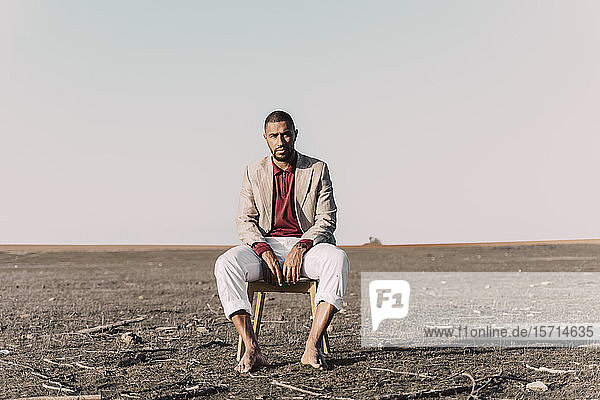 Portrait of young man sitting on chair in barren land