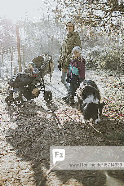Mother with daughters and border collie during forest walk in autumn