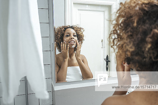 Junge Frau im Badezimmer trägt Gesichtscreme auf