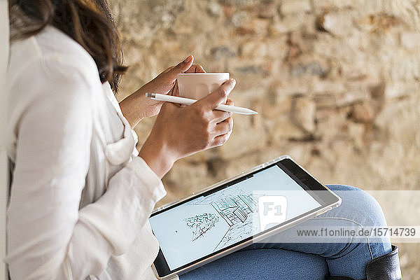 Schnittansicht eines jungen Architekten mit Kaffeetasse bei der Arbeit am digitalen Tablett