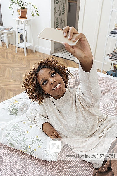 Happy young woman lying in bed taking a selfie
