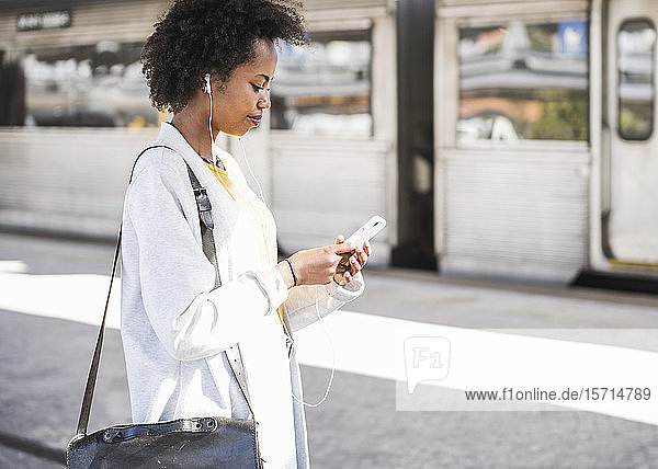 Junge Frau mit Handy und Kopfhörern am Bahnhof