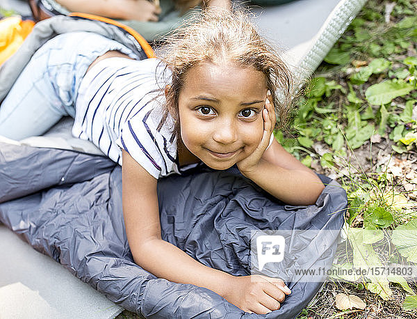 Kleines Mädchen liegt auf einem Schlafsack und schaut in die Kamera