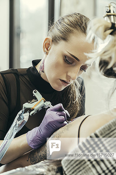 female tattooist tattooing upper arm of female customer