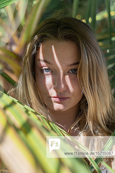Porträt einer blonden jungen Frau zwischen Palmenblättern