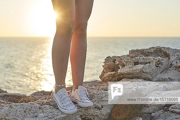 Beine einer jungen Frau  die auf einer Klippe am Meer steht