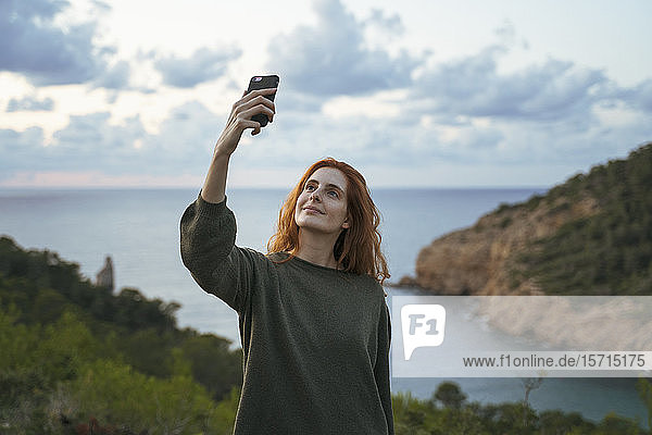 Redheaded young woman taking a selfie at the coast  Ibiza  Spain