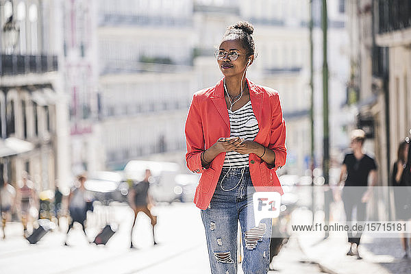 Junge Frau mit Kopfhörern und Smartphone  die sich in der Stadt umsieht  Lissabon  Portugal